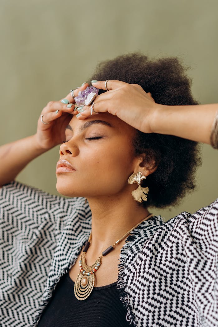 African American woman with afro hair holding an amethyst crystal, eyes closed in meditation.
