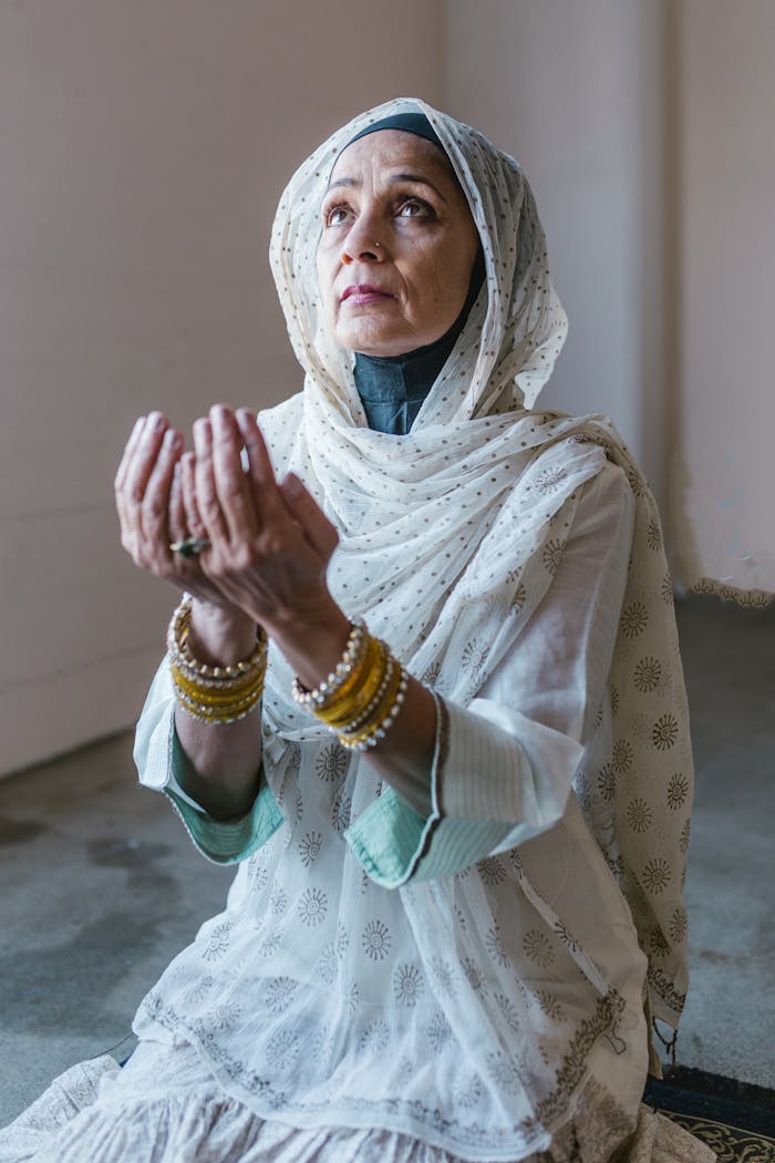 Senior woman in traditional attire praying indoors, embodying faith and devotion.